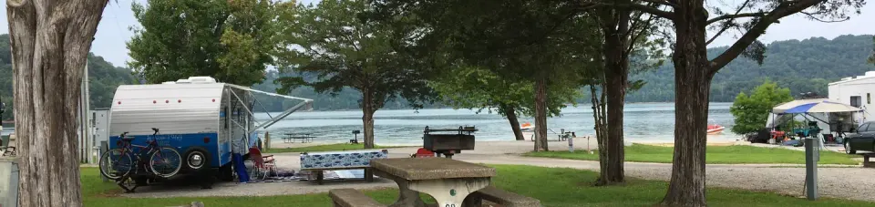 OBEY RIVER PARK CONCRETE TABLE IN FOREGROUND, CAMPER ON LEFT AND LAKE IN BACKGROUND