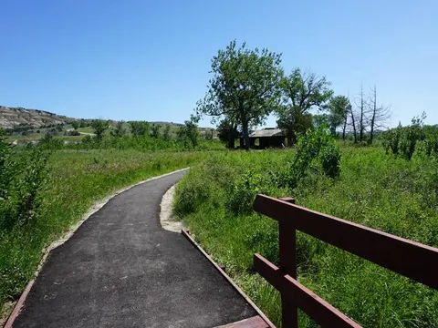 Paved trail leading to a building in a lush, green field.