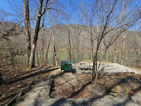 A green food storage locker sits near a picnic table on a campsite overlooking the river.