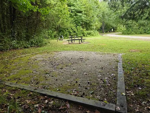 A square gravel tent pad can be seen in the foreground with a picnic table behind it.