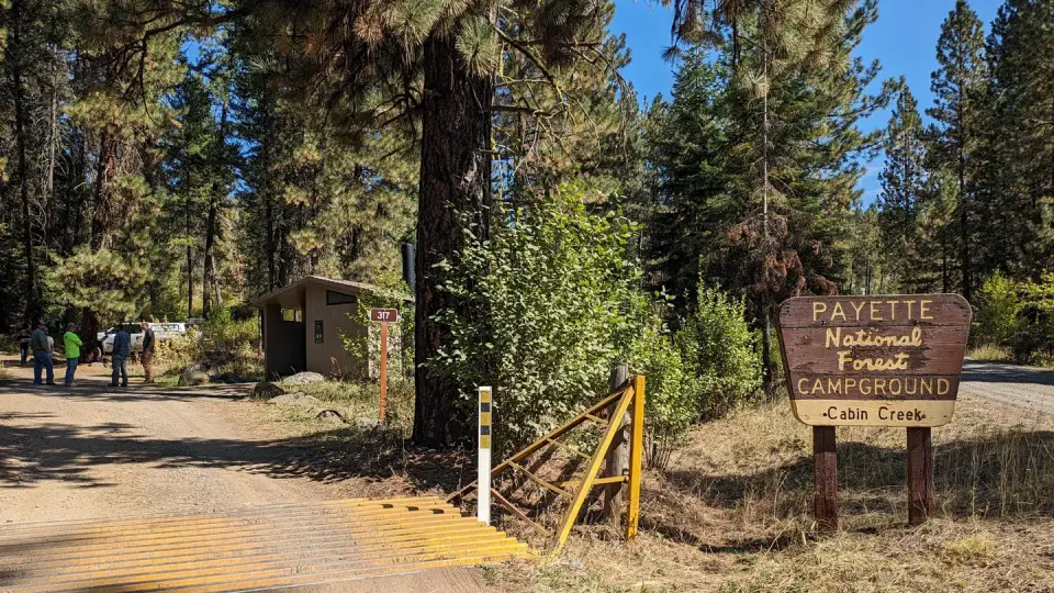 Sign at entrance to campground with tall conifer trees.