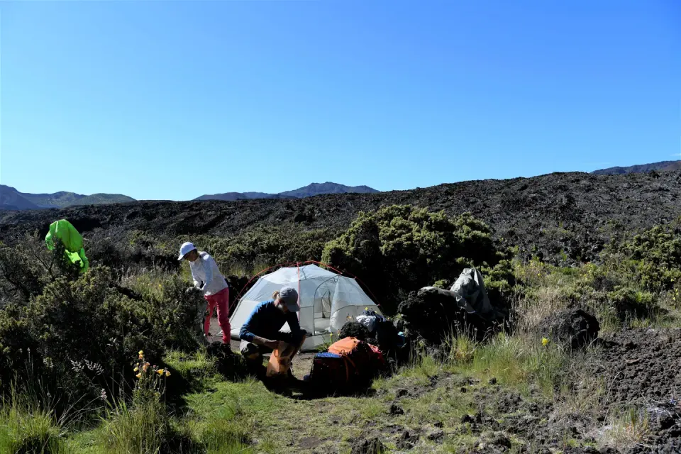 two campers pack up their camp with tent among grass and lava field
