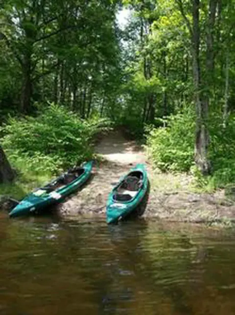 Two green kayaks on shore of river with trees in the background