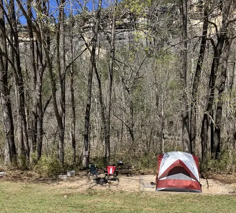 A red and gray tent sits on a tent pad at Kyles Landing Campground with two chairs to the left.