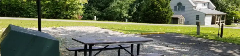Picnic table sits on gravel tent pad with bathhouse in background