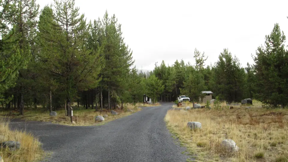 View of east part of campground including gravel road, campsite, toilet, fee station and white truck