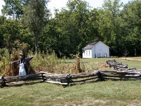A historic one room schoolhouse at Alley Spring with garden and scarecrow in the foreground
