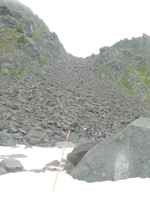 Steep rocky incline with five hikers at the base.