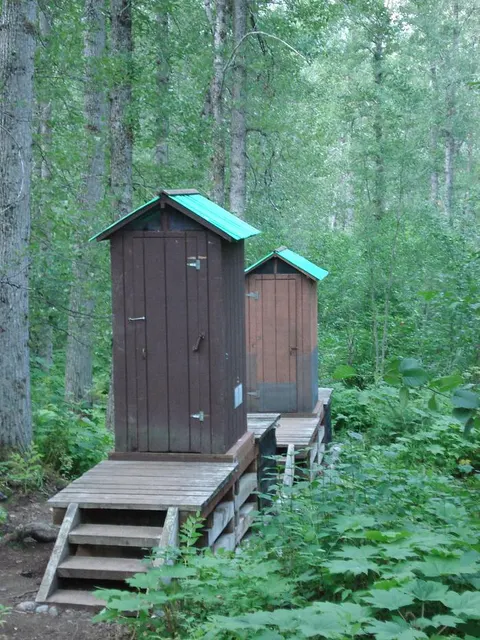 Two small outhouse buildings in a forested area.