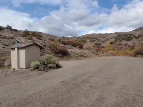 A view of the dirt parking area and vault toilet as you enter the group site