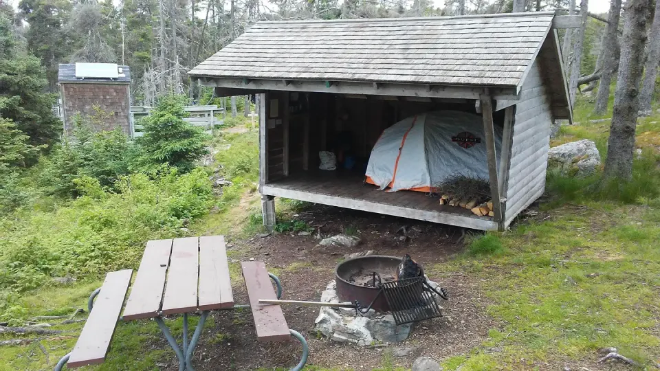 Tent shelter, fire ring and picnic table on grassy hillside.