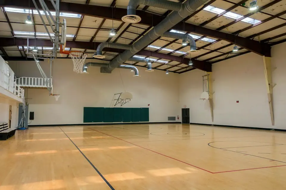 Interior view of gymnasium. Standard size wooden marked floor with 6 basketball backboards/nets.