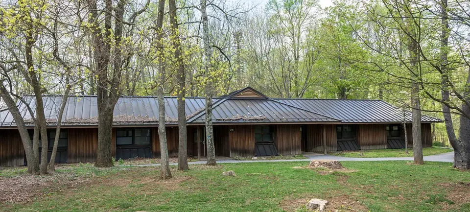 Front view of one dormitory building in early spring. Large trees are visible in front and behind the dormitory. Each dorm accommodates 30 people and is heated.