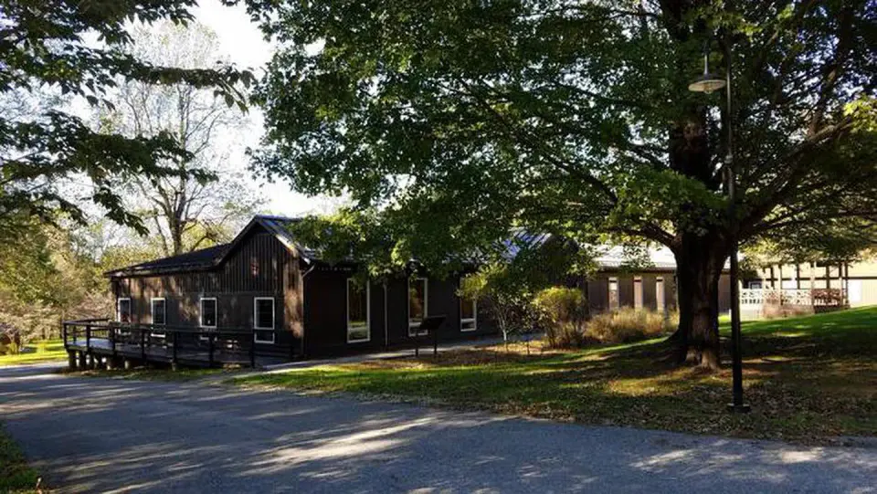 Dining Hall building front entrance view showing wooden gazebo and maple tree. Side of building has wooden accessibility ramp.
