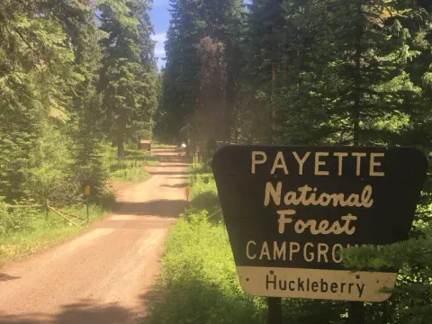 Dirt road with forest alongside and large sign for Huckleberry Campground.