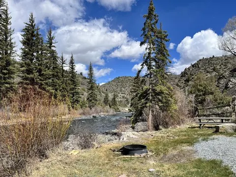 River through mountainous terrain, forested and rocky. Picnic table and fire pit