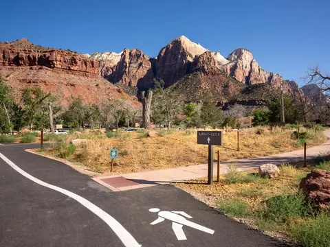 Pedestrian path winding through the campground with sheer, dramatic sandstone cliffs of Zion Canyon rising in the background.
