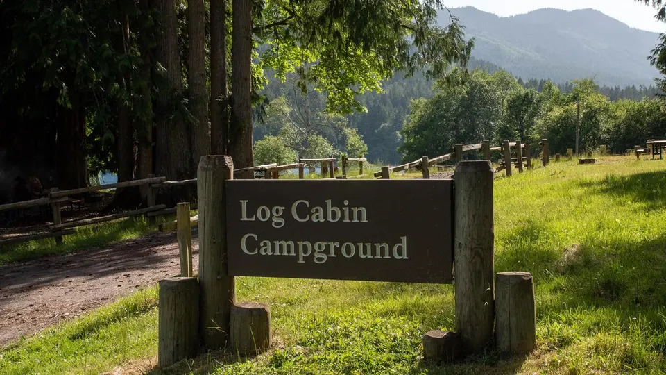 The wooden entrance sign for Log Cabin Campground surrounded by beautiful trees.