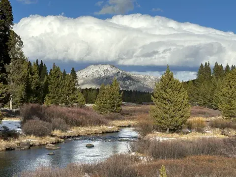 Bunsen Peak under cumulus clouds with a creek in the foreground.
