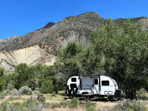 Cimarron Campground campsite with recreation trailer, picnic table, fire pit, mountain, trees, and sagebrush covered peak in the background.