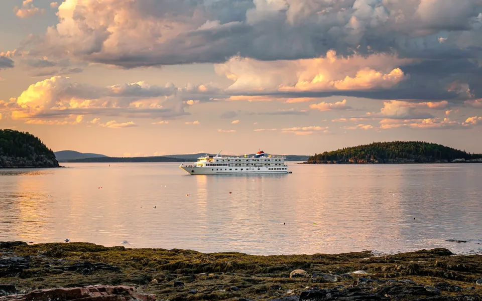 A luxurious cruise ship sailing tranquil waters under a dramatic cloudy sky at sunset.
