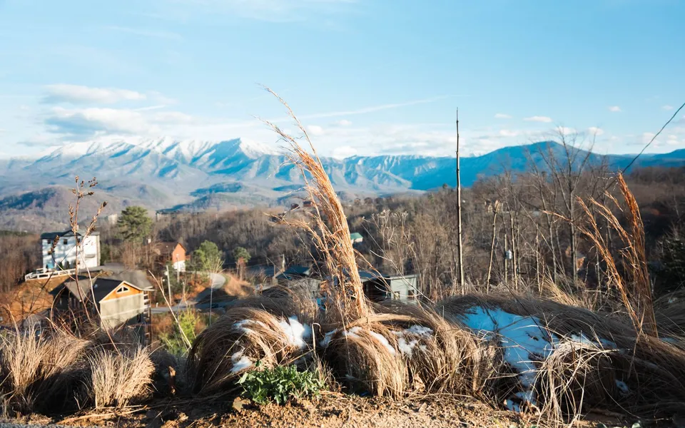 Picturesque landscape of snow-covered mountains, countryside homes, and dry grass in early winter.