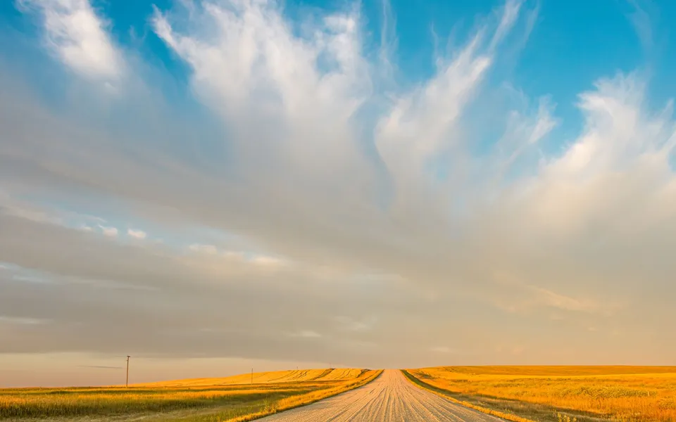 A vast prairie landscape in Saskatchewan with a rural road and dramatic clouds at sunset.
