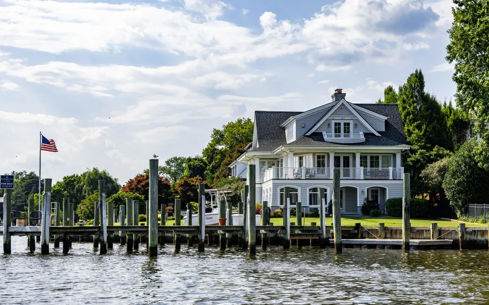 A lovely waterfront home with a dock and American flag on a sunny summer day.