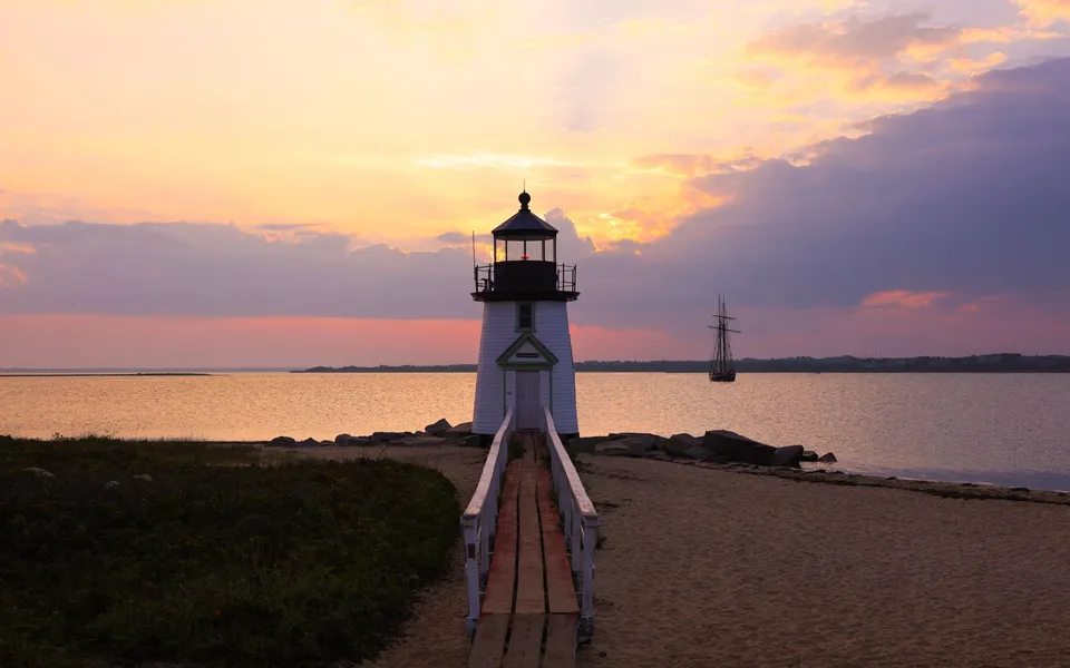 Silhouetted lighthouse at sunset with a tranquil sea in the background.