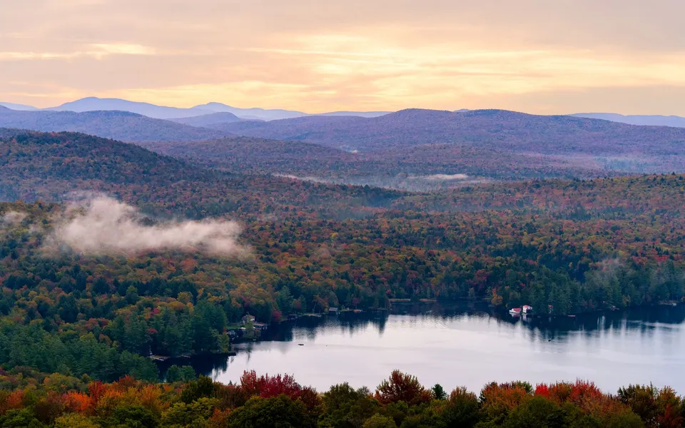 Breathtaking view of Adirondack Mountains with vibrant autumn colors at sunrise over a serene lake.