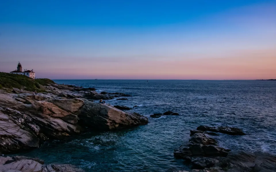 Beautiful sunset over the ocean with Beavertail Lighthouse and rocky shoreline in Jamestown, RI.